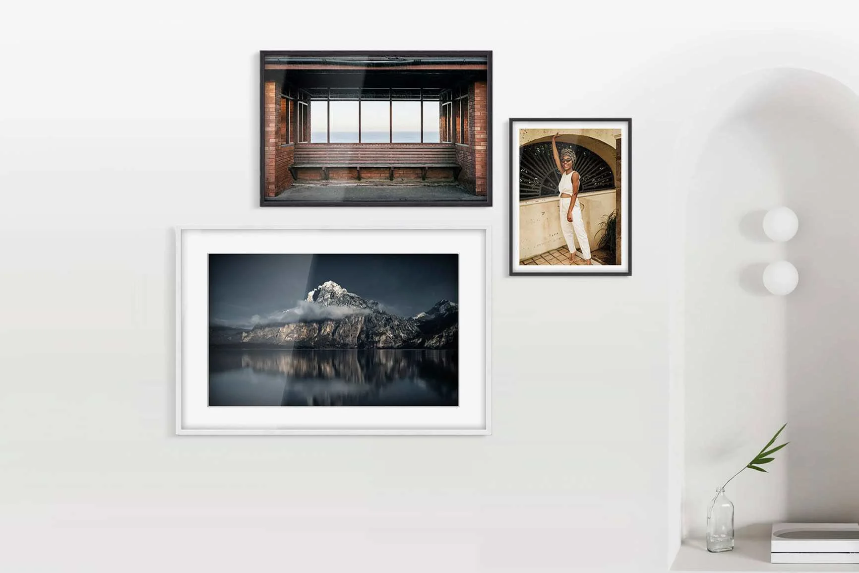 Drei Vitrinenrahmen an weißer Wand: oben links Fensterfront mit Backsteinmauer, rechts Porträt einer Frau, unten Berg mit See.