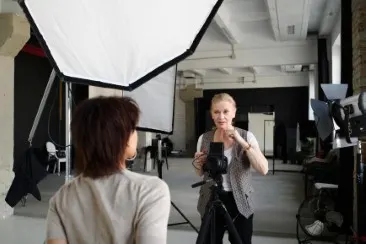 Photo studio with professional lighting and camera on a tripod, two people during a photo shoot.