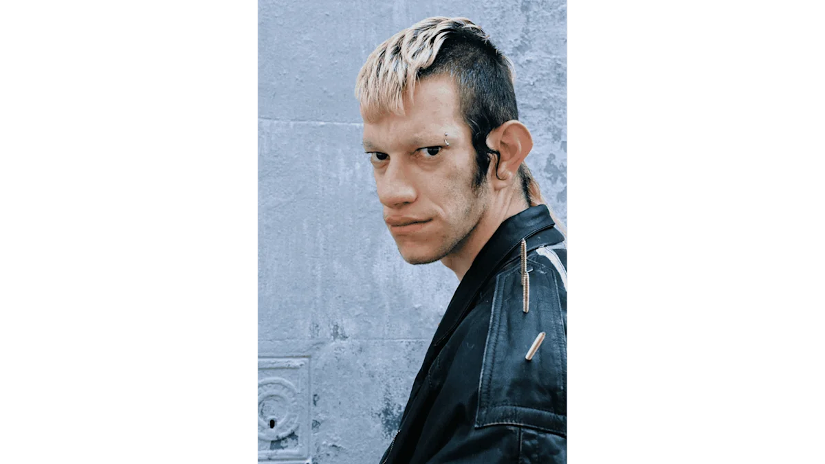 Portrait of a man with short hair and dyed blond hair with nails on the shoulders of his leather jacket