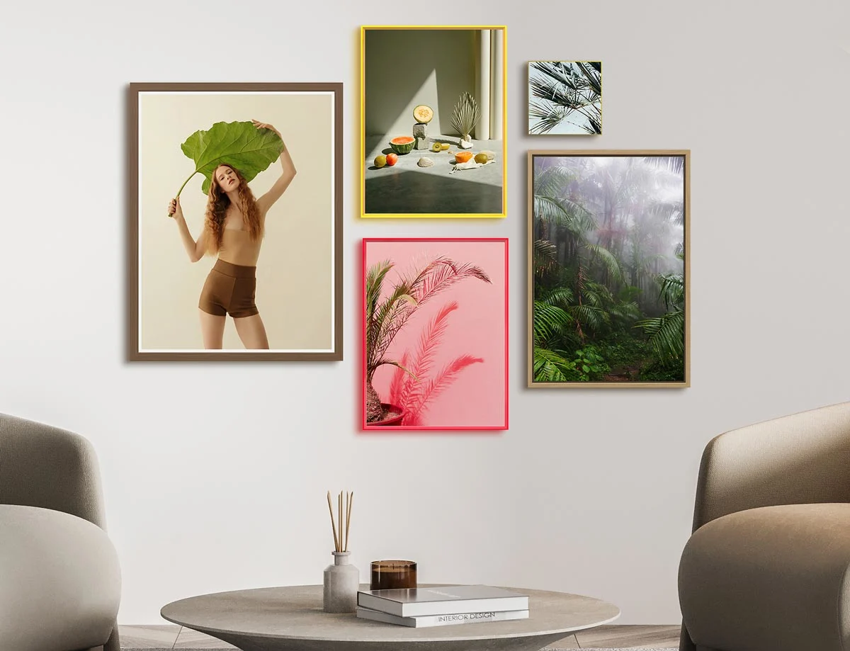 Five framed pictures in different colors and sizes on one wall. The motifs include a woman with a large leaf, fruit on a table, palm leaves and a dense forest.