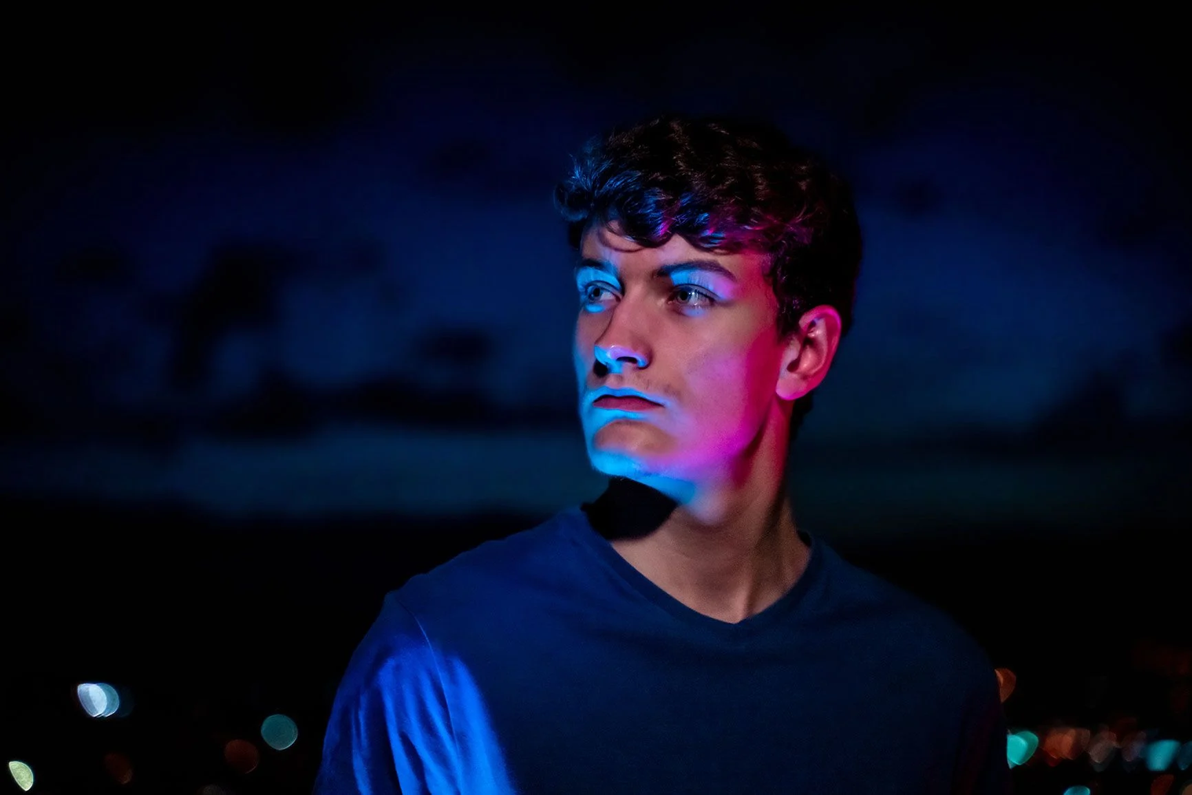 A portrait of a man against a dark background, his face illuminated by blue and pink RGB light.