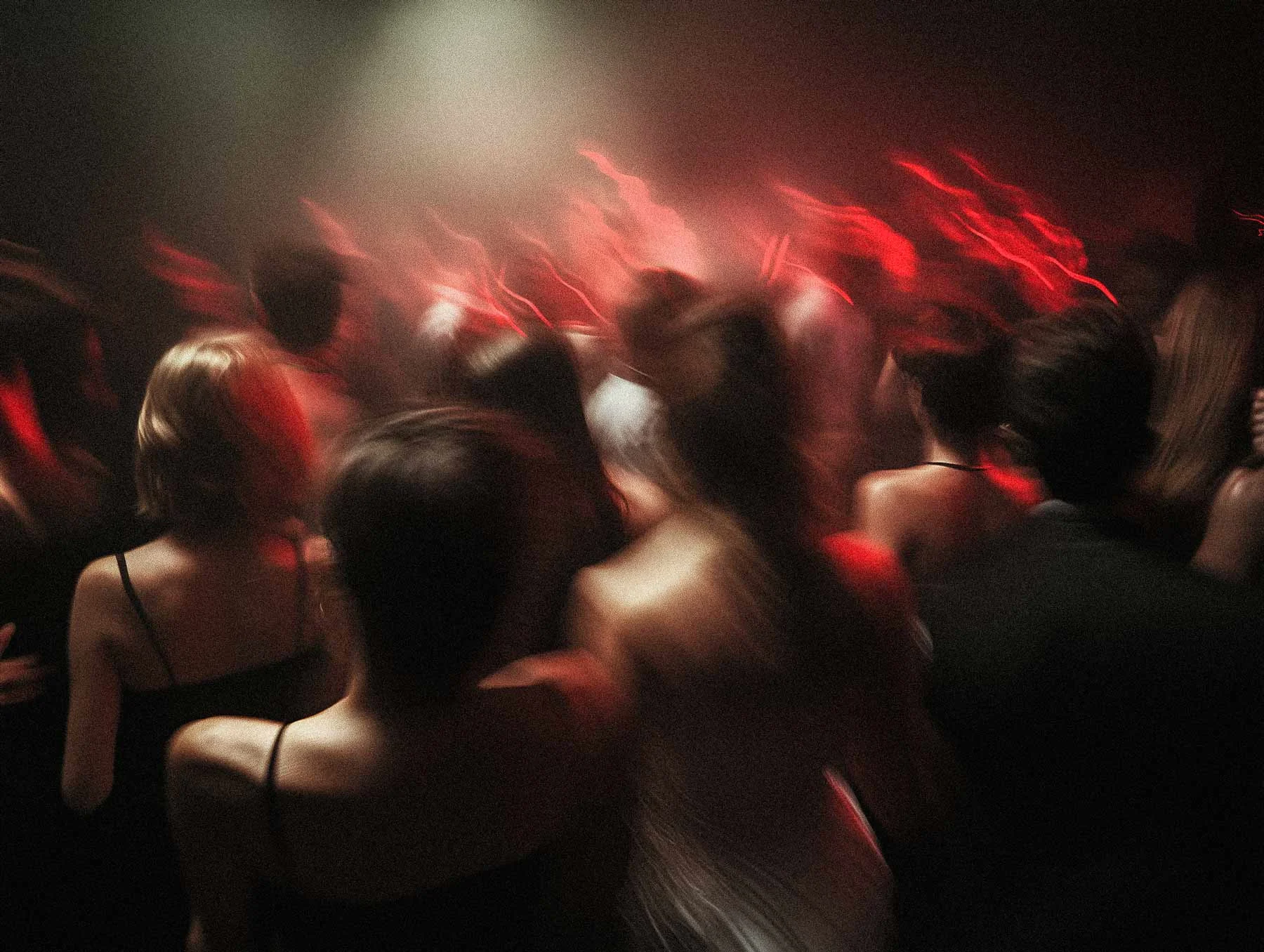 People are dancing in a dark room with red lighting, their movements blurred.