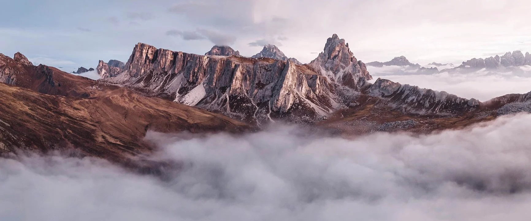 A mountain range with rugged peaks rising above a blanket of clouds in subdued light.