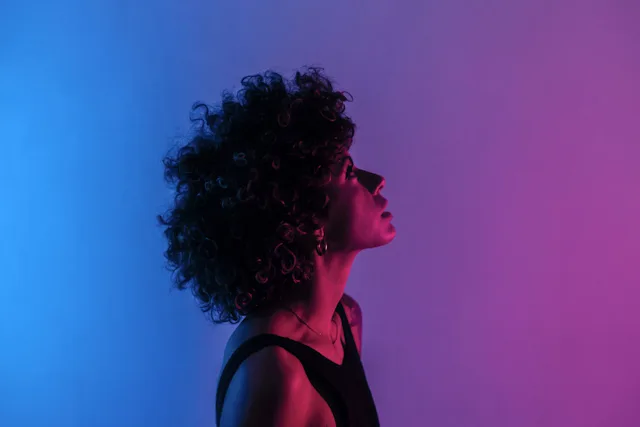 Portrait of a woman with curly hair, shown in profile against a blue-violet background with color filters.
