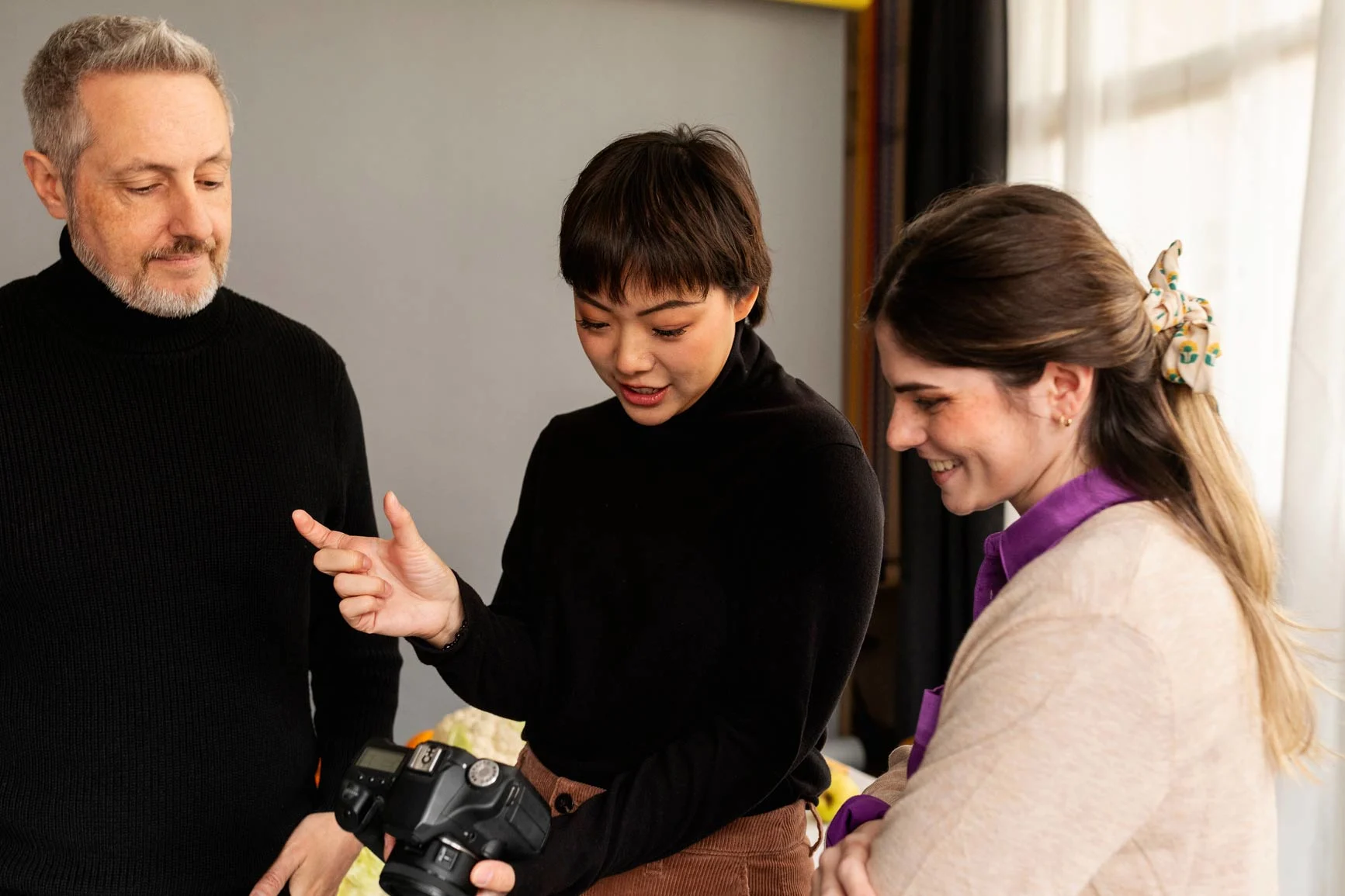 Three people stand together, one person holds a camera in their hands and shows something on it while the other two people watch.