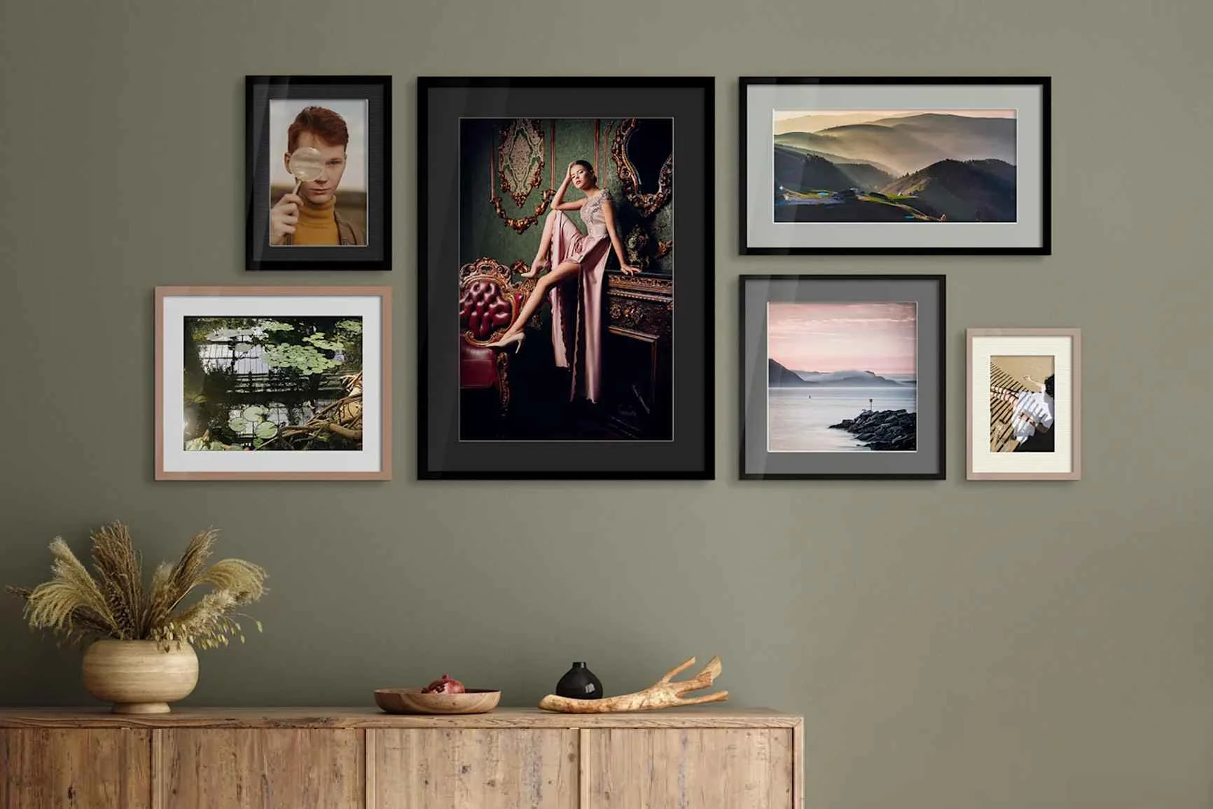 Parete con sei quadri incorniciati con motivi diversi sopra una credenza in legno decorata con piante essiccate e pezzi di legno.