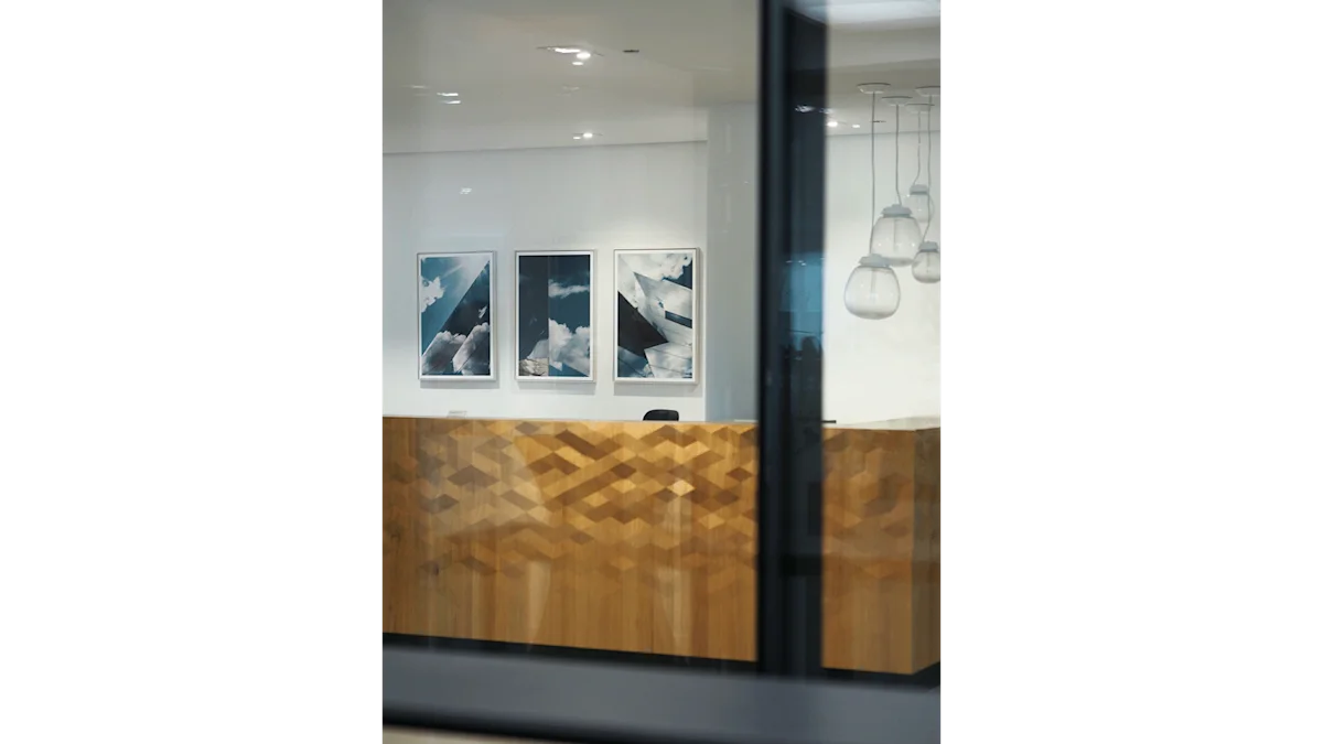 A modern office reception desk with wood geometric paneling, three framed architectural photos on the wall, and pendant lights overhead.