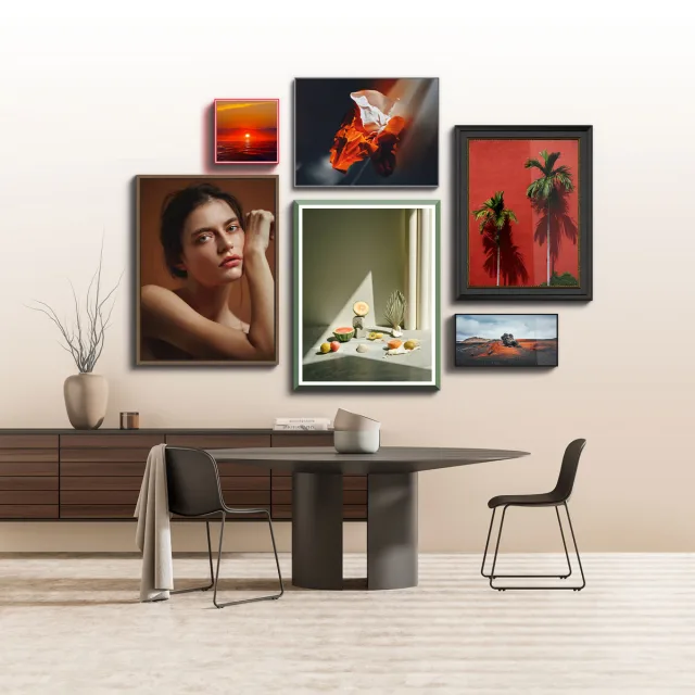 Several pictures in different frames and sizes are arranged on a bright wall above a modern table.