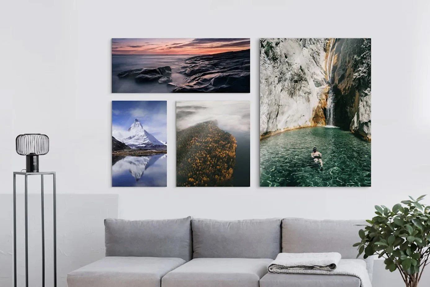 Vier Wandbilder mit Naturmotiven über einem grauen Sofa an einer weißen Wand mit Deko und Pflanze.