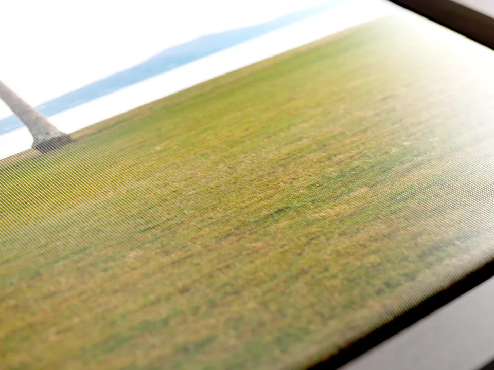 Gros plan d’une impression sur toile textile représentant une image d’un champ d’herbe verte sous un soleil éclatant, avec un ciel bleu.