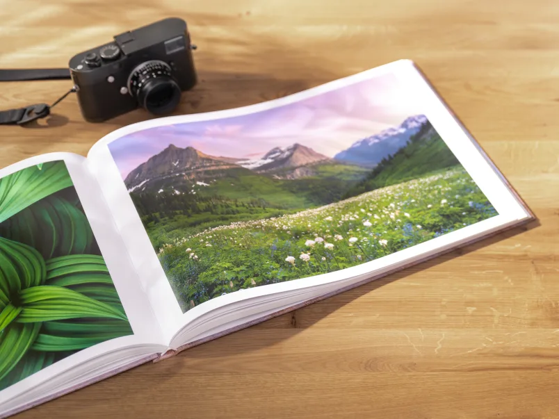 An open coffee table book lying on a table with a camera next to it