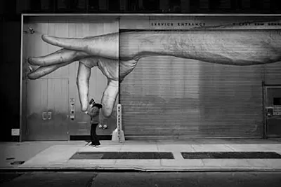 Street art of a person standing under a graffiti painting of a hand.
