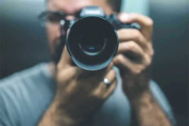 Portrait of a man with a camera with a large lens in front of his face.