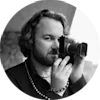 Schwarz-weißes Porträt eines Fotografen, der eine Kamera im Vintage-Stil hält, ein dunkles Hemd und eine Perlenkette trägt