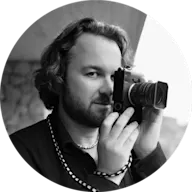Schwarz-weißes Porträt eines Fotografen, der eine Kamera im Vintage-Stil hält, ein dunkles Hemd und eine Perlenkette trägt