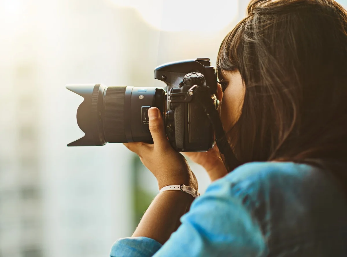 Woman with long dark hair holds a DSLR camera close to her face to take a photo.