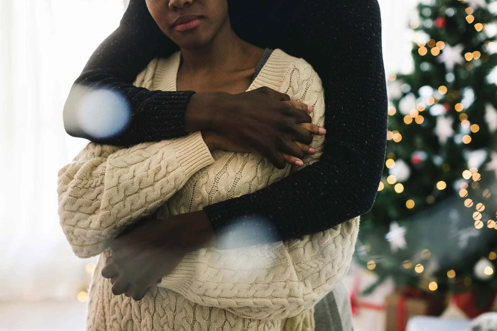 Zwei Personen umarmen sich,  im Hintergrund ein geschmückter Weihnachtsbaum.