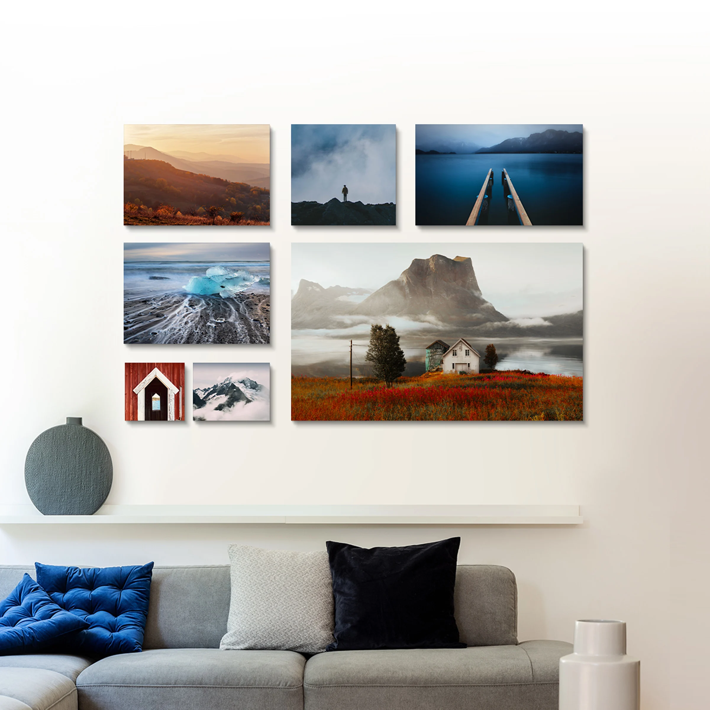 Sette fotografie paesaggistiche di diverse dimensioni disposte su una parete sopra un divano grigio.