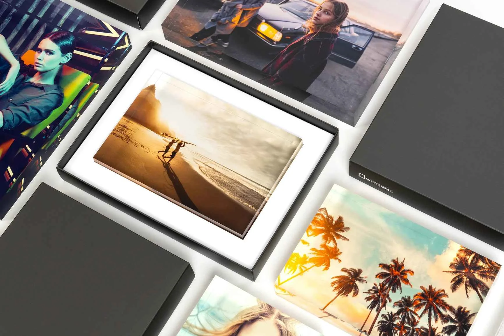 Blocco fotografico in acrilico con confezione regalo, circondato da altri blocchi fotografici in acrilico con diversi motivi, come spiaggia, palme e persone.