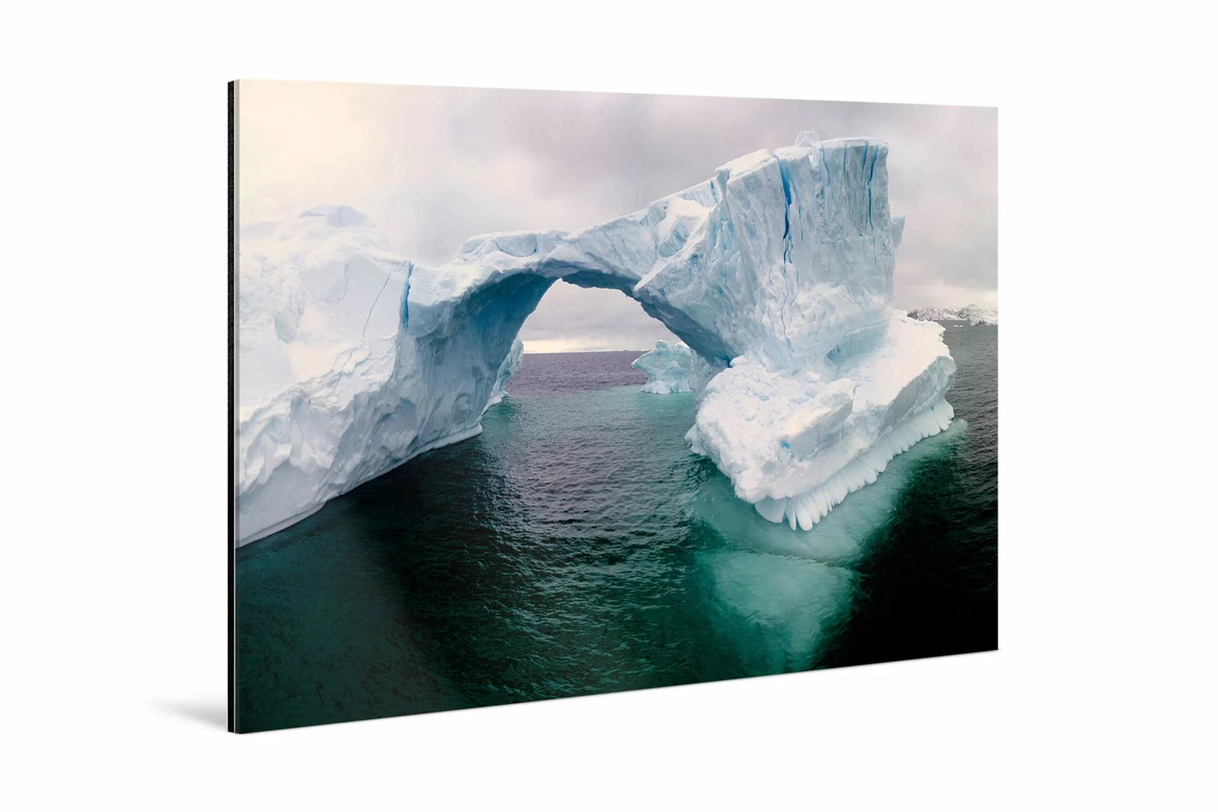 Großer Eisberg mit natürlicher Brückenform über dunklem Wasser unter bewölktem Himmel.