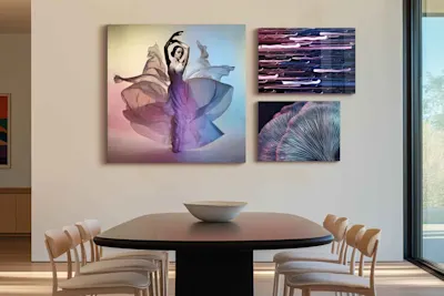 Three photos framed behind acrylic glass on a wall above a dining table with six chairs.