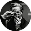 Ein bärtiger Fotograf in dunkler Kleidung macht ein Foto mit einer klassischen Messsucherkamera im kreisförmigen Schwarzweiß-Porträtformat