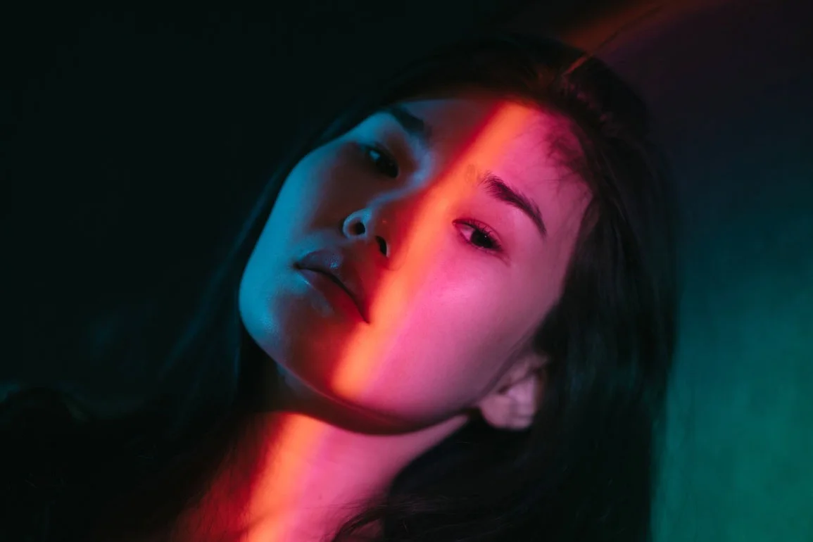 Portrait of a woman with long hair against a dark background, illuminated by red and green light.