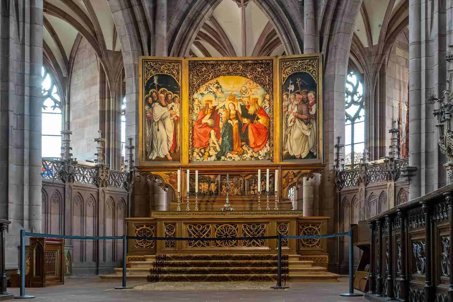 Trittico con raffigurazioni religiose su un altare in una chiesa con alti archi a sesto acuto e pannelli in legno decorati.