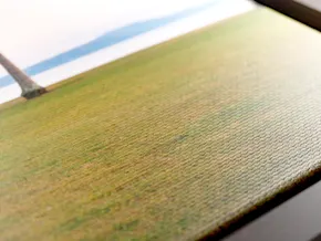 Gros plan d’une impression sur toile brillante représentant une scène de plage avec de l’herbe verte, un océan bleu, des vagues blanches et le tronc d’un palmier.