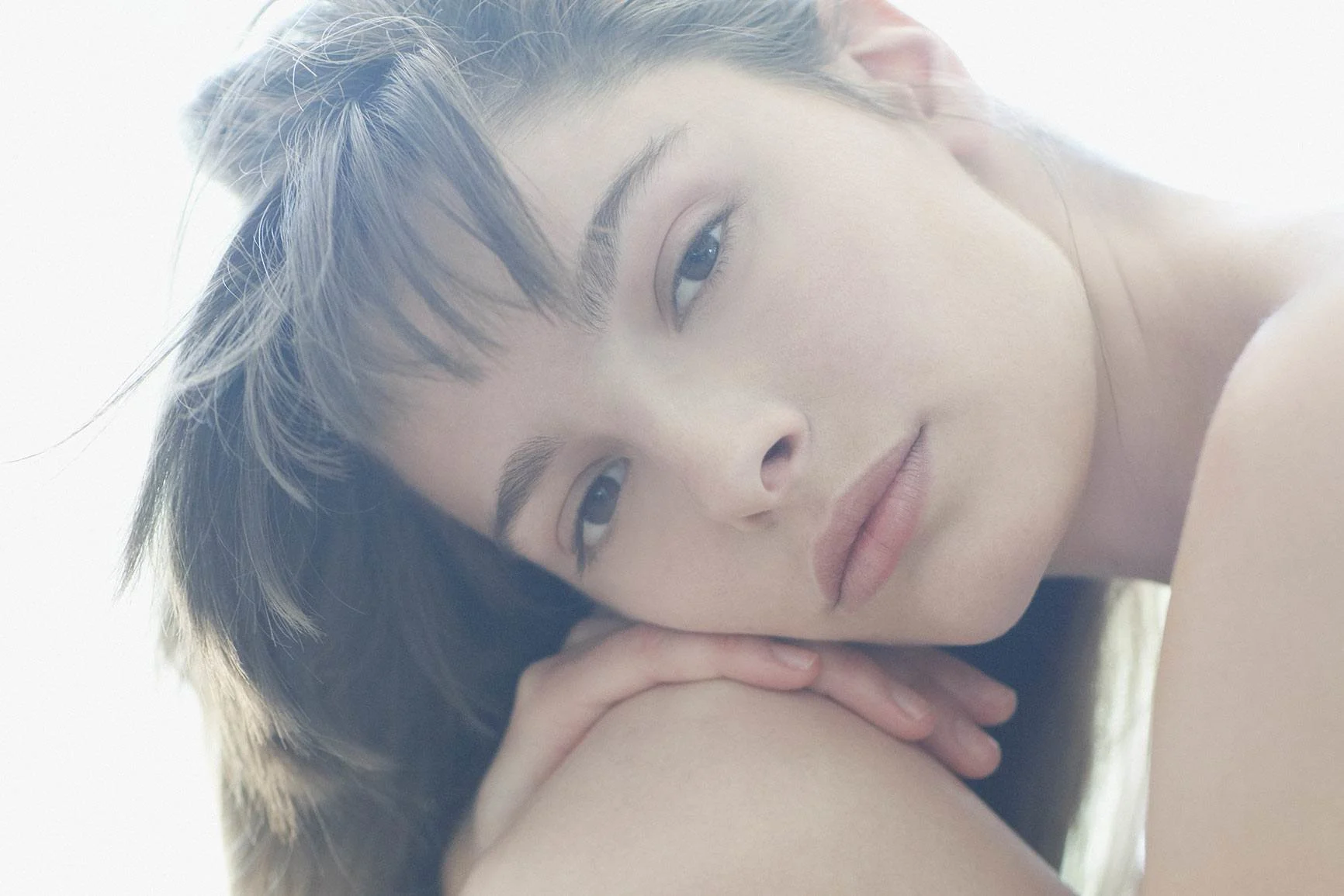 Porträt einer Frau mit langen Haaren, die ihren Kopf auf die Knie gestützt hat.