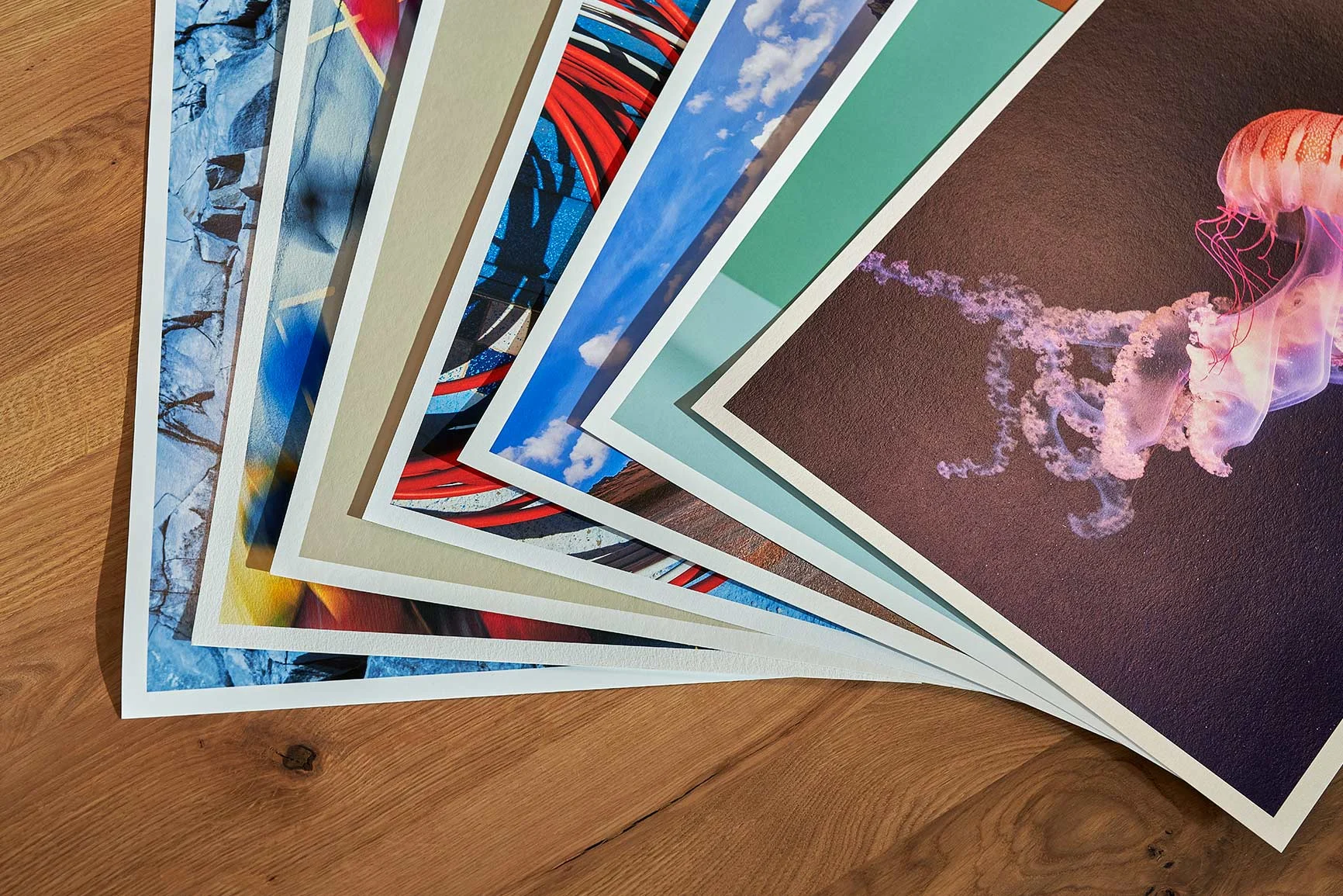 Mehrere Fine Art Prints mit weißen Rändern liegen auf einem Holztisch.