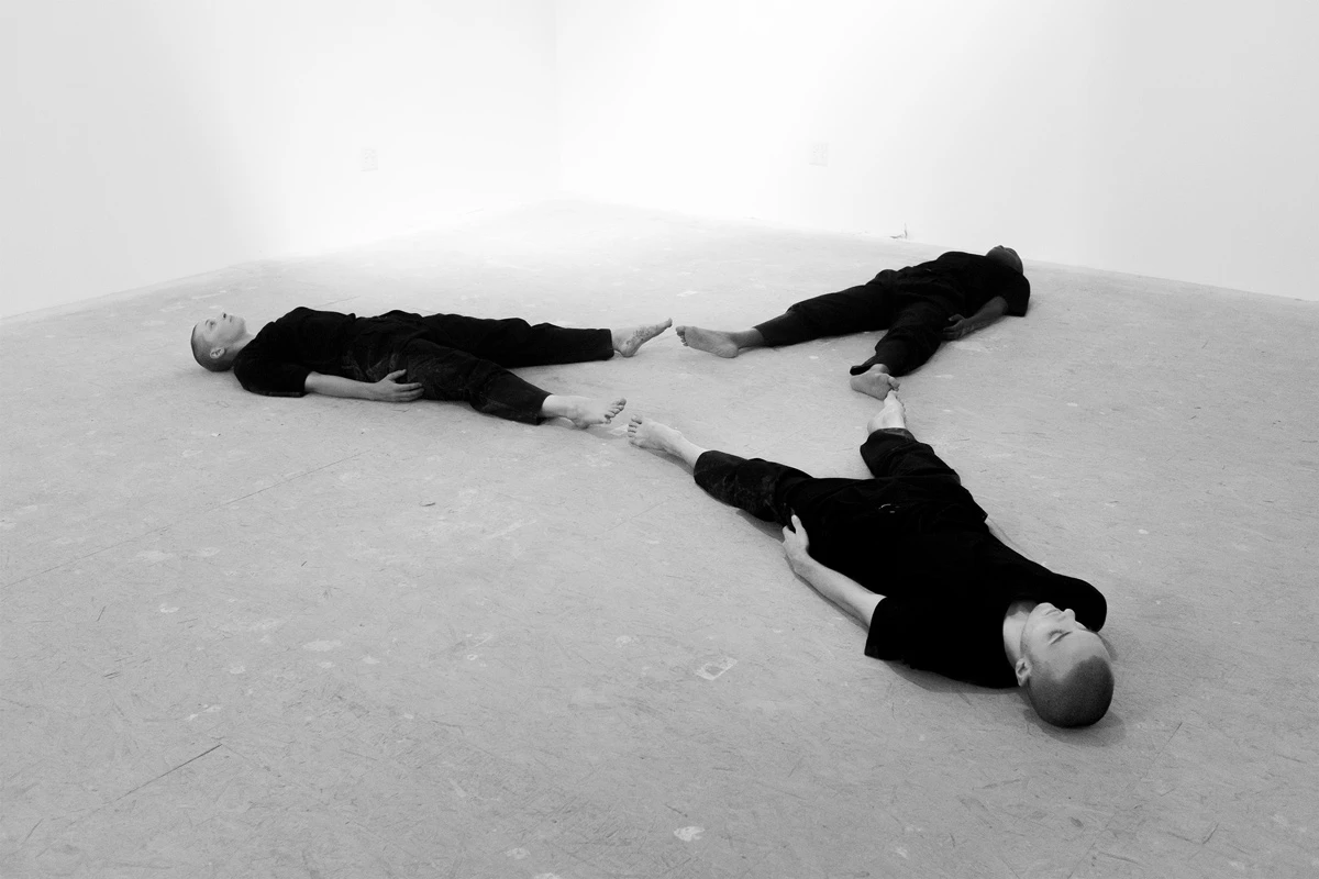 Black and white photo of three people lying on the ground lined up in geometric form.