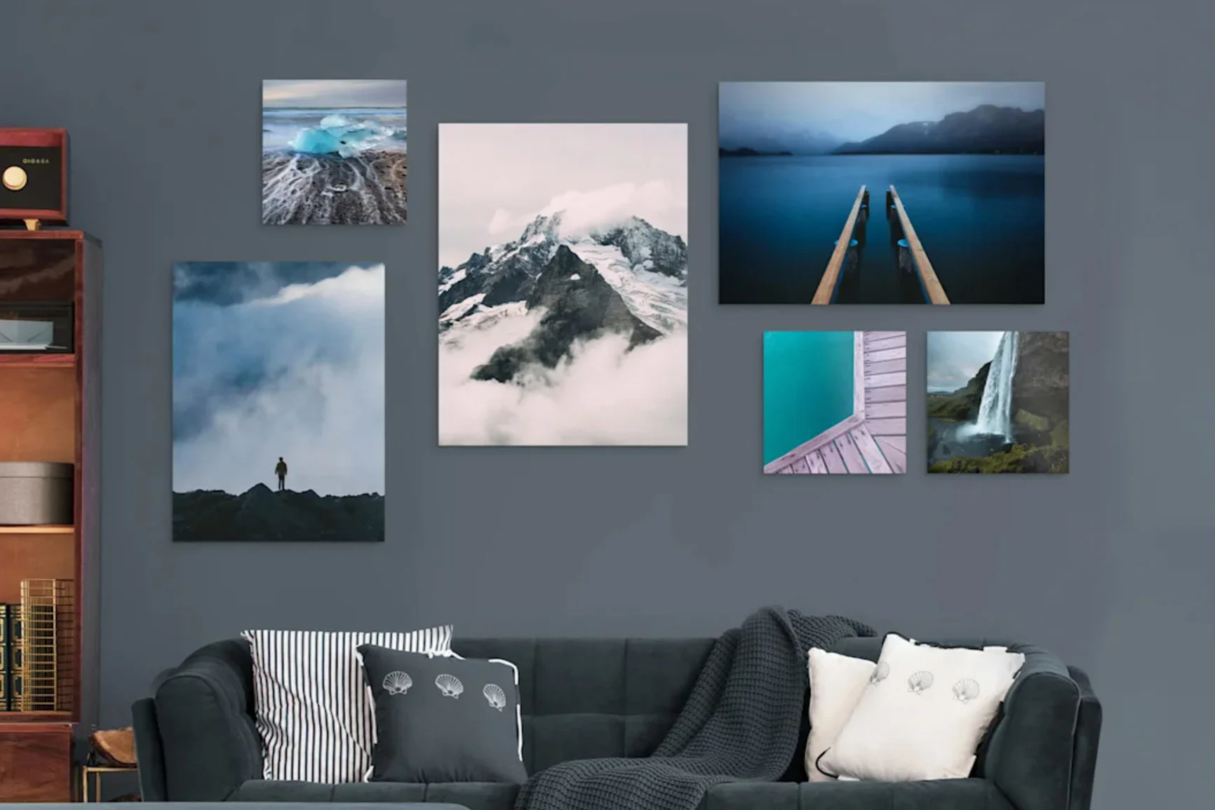 Soggiorno con divano grigio scuro, diversi cuscini e cinque fotografie paesaggistiche di diversi formati appese alla parete scura.