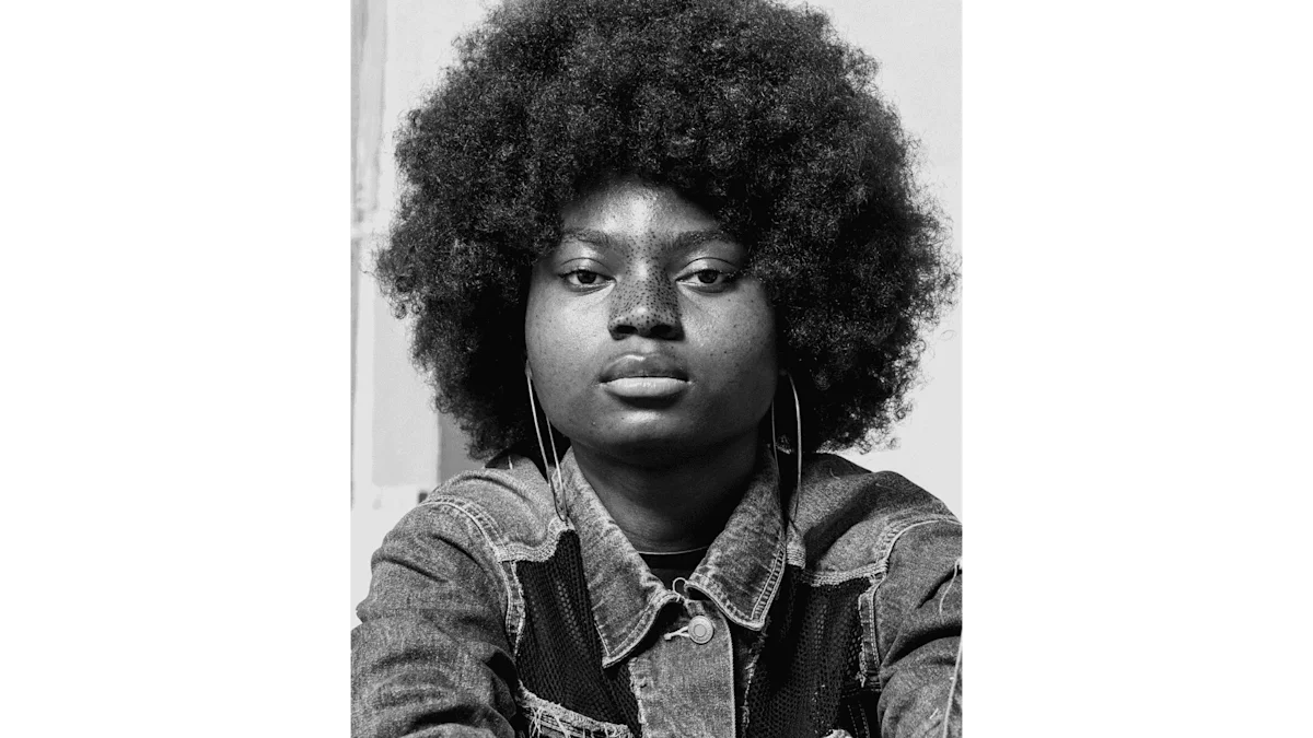 Portrait en noir et blanc d'une femme avec une coupe afro et des taches de rousseur.