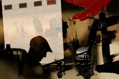The silhouette of a man wearing a hat in front of a wall with shadows and abstract red and black brushstrokes. Part of a car is visible.