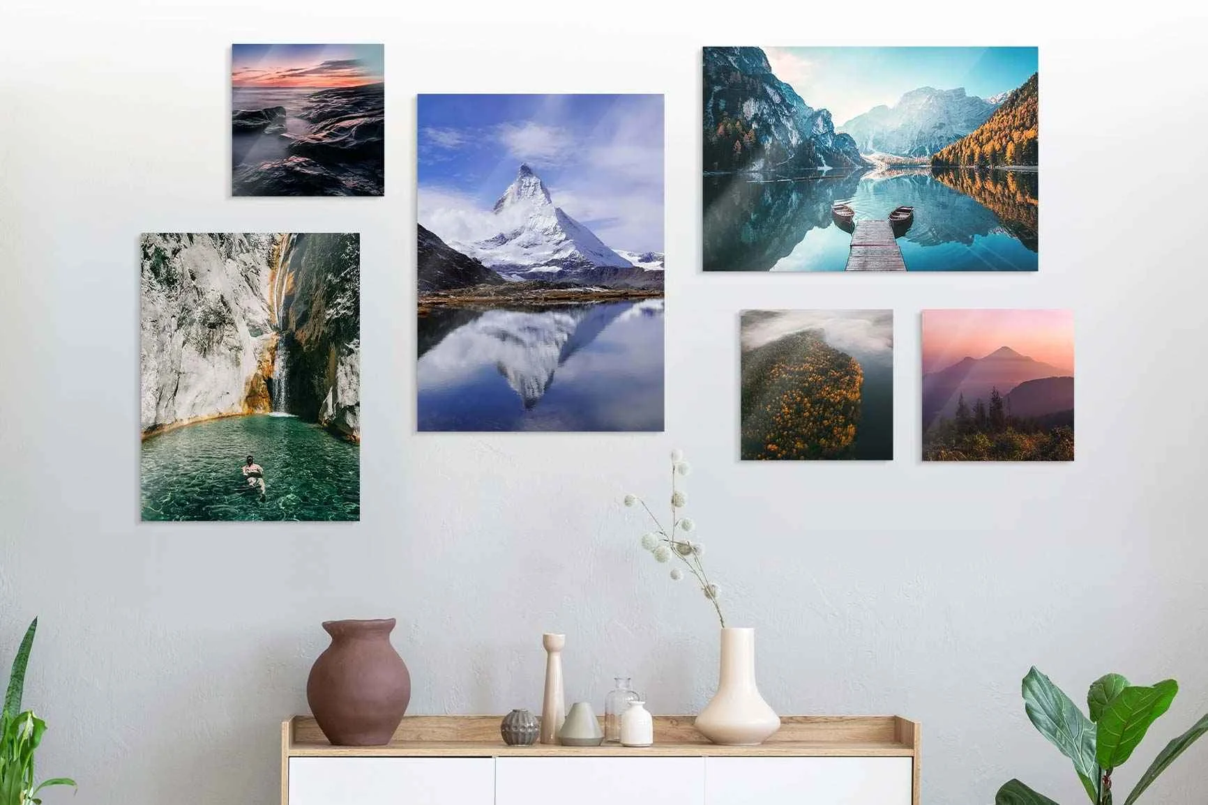 Parete con sei fotografie paesaggistiche sopra una credenza con vasi e piante.