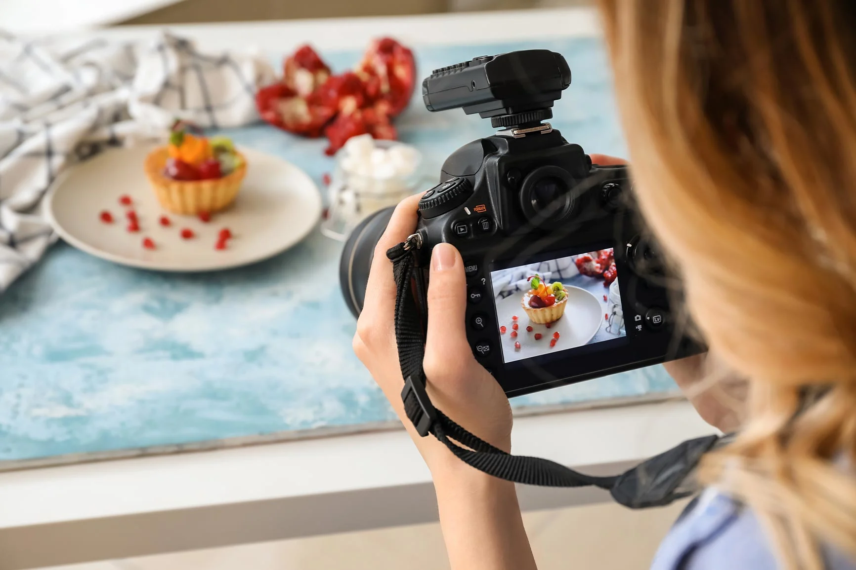 A person is taking a photo of a dessert on a white plate against a light-colored background.
