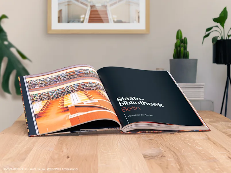 Open fotoboek op een houten tafel, met foto's van de Staatsbibliotheek van Berlijn; planten en fotolijst op de achtergrond.
