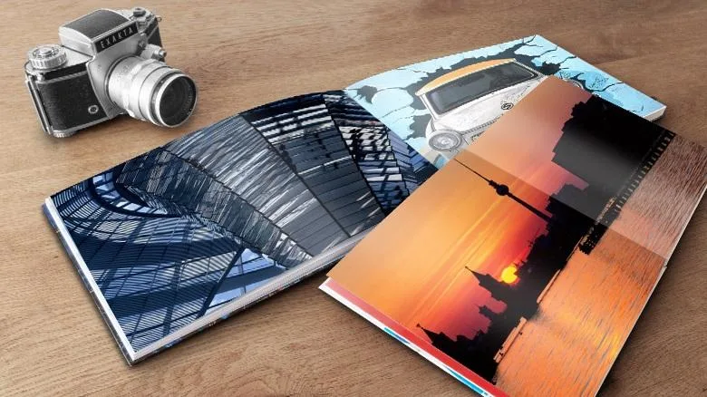 Zwei geöffnete Fotobücher mit Architektur- und Stadtbildern auf einem Holztisch, daneben eine Kamera.