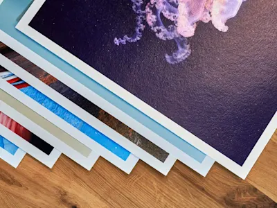 Più stampe artistiche con bordi bianchi su un tavolo di legno, quella superiore mostra un'illustrazione di medusa viola.