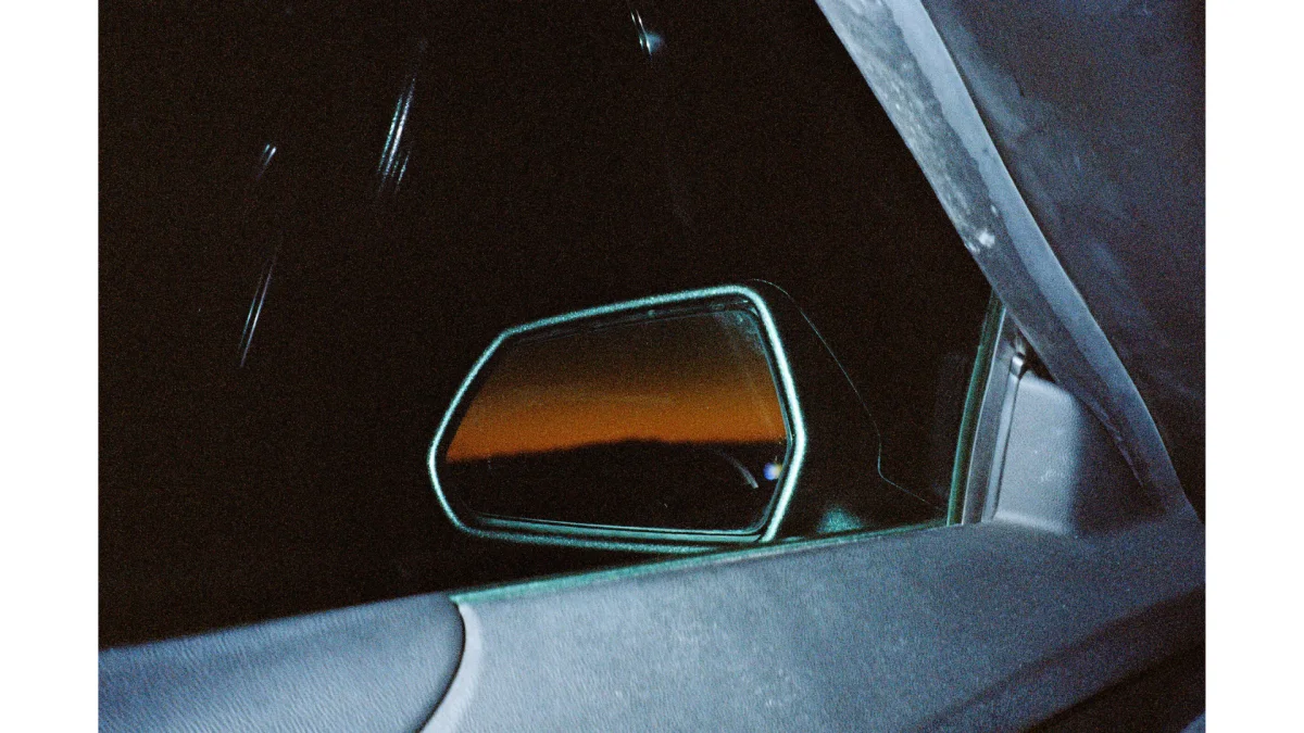 photo of a rear-view mirror taken from inside a car. The landscape is visible in the rearview mirror.