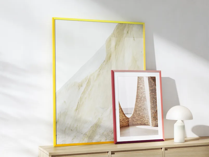Zwei Design-Edition-Rahmen in Gelb und Violett, die auf einem Sideboard stehen.