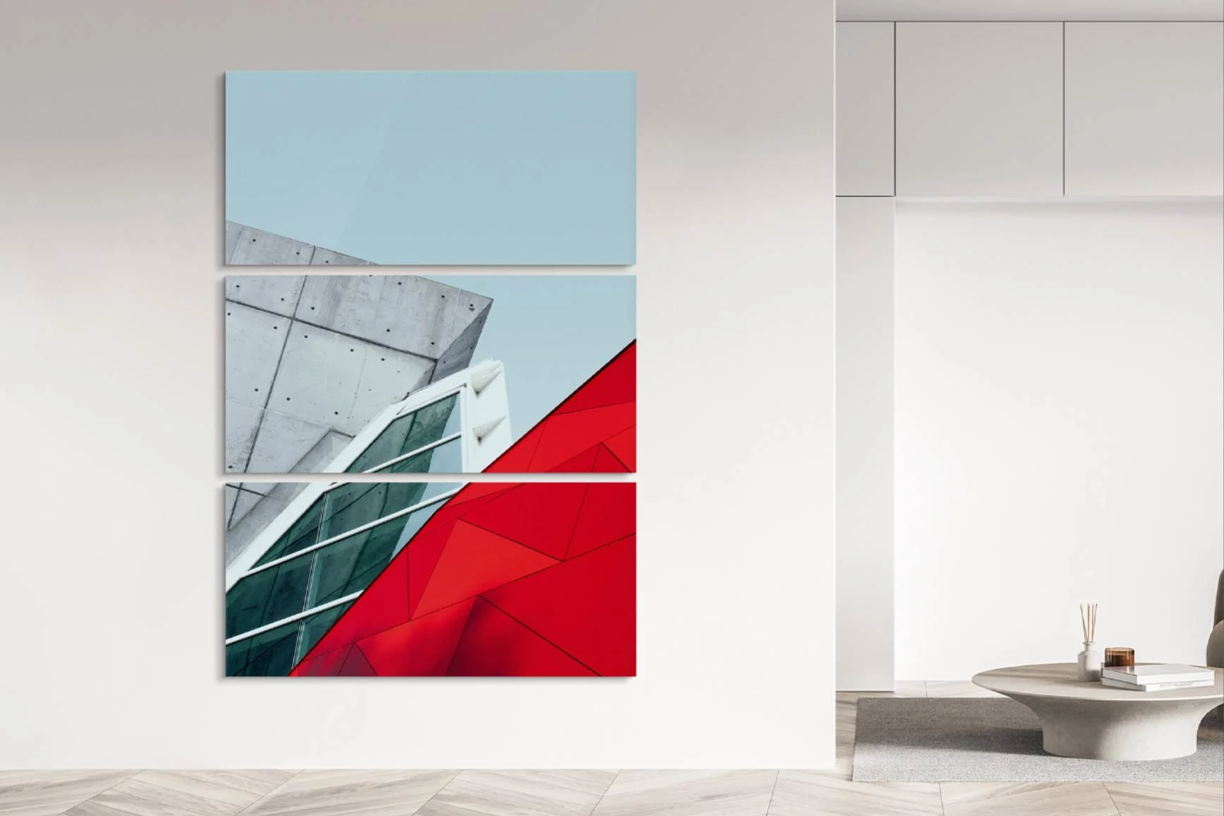 Trittico con forme architettoniche astratte in blu, grigio, bianco e rosso su una parete bianca in uno spazio moderno.