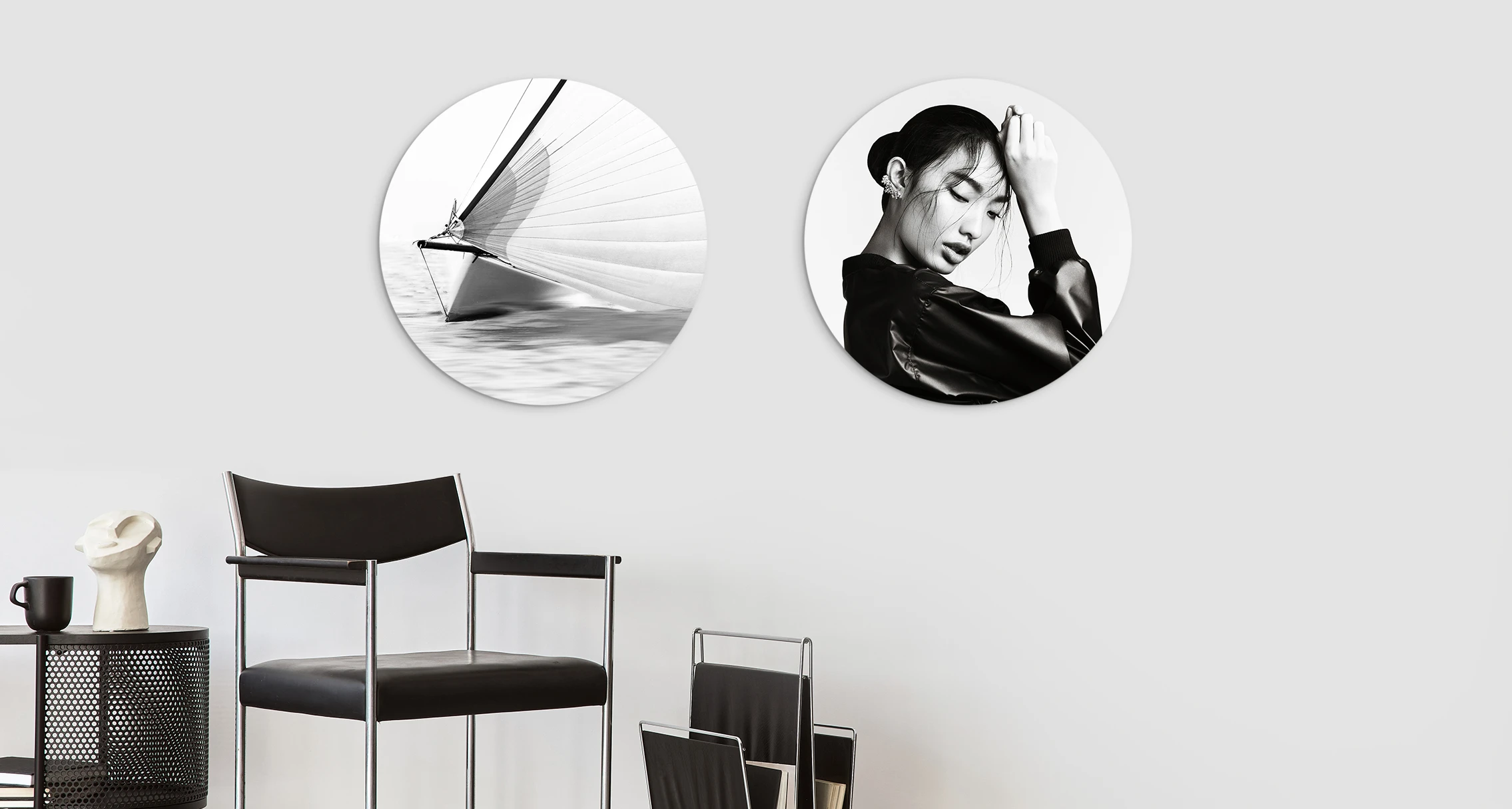 The motifs of a woman and a sailboat in black and white can be seen on 2 different round pictures that are hung side by side on a wall. 