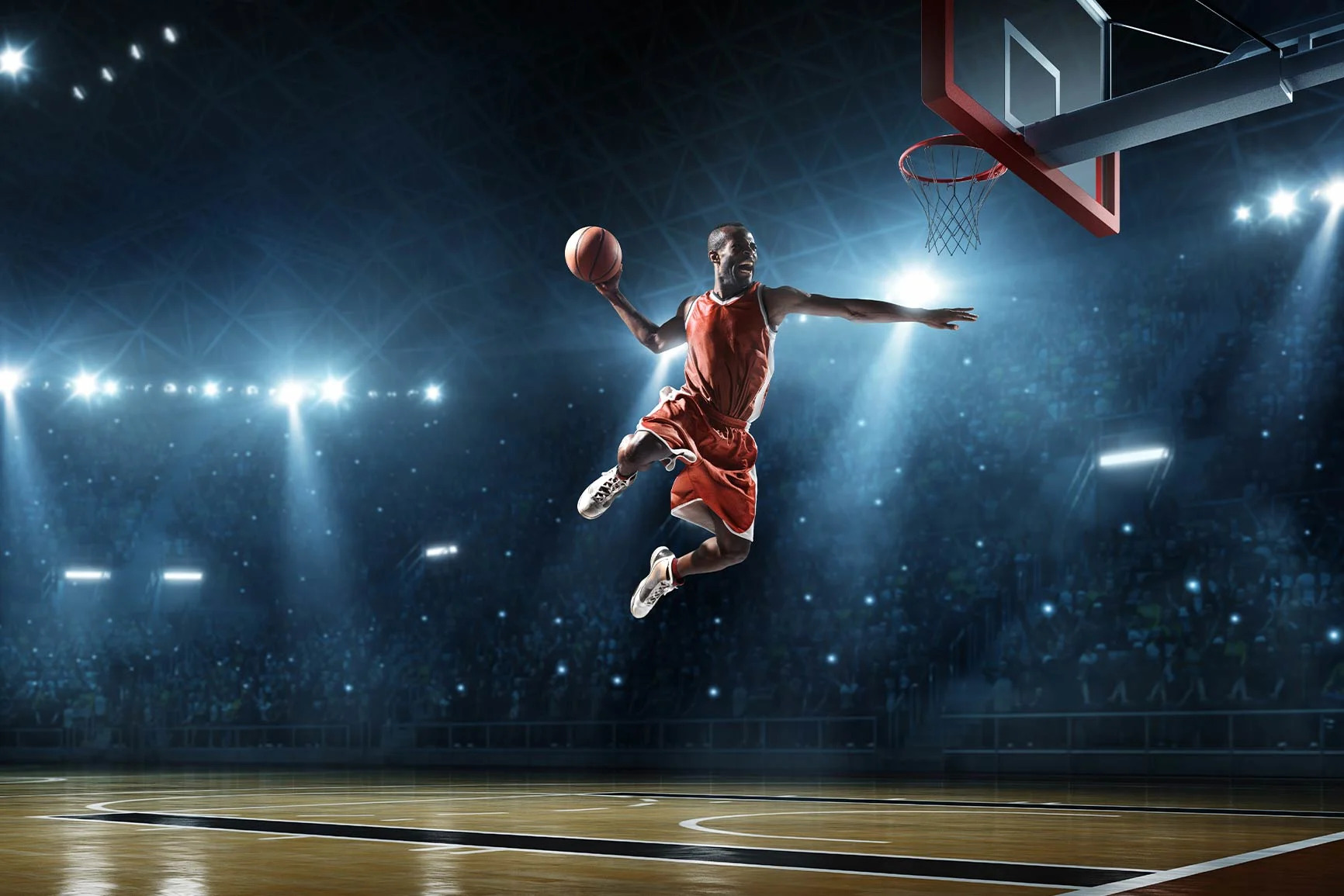 A basketball player in a red jersey jumps to dunk the ball in a large arena with a crowd in the background.