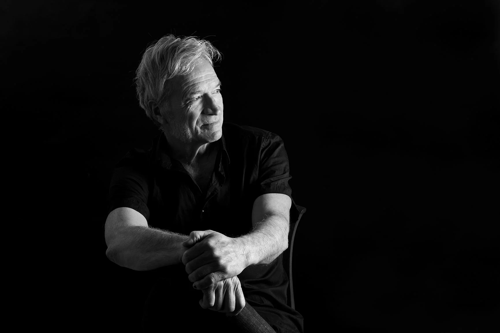 A low-key portrait of a seated man against a black background.