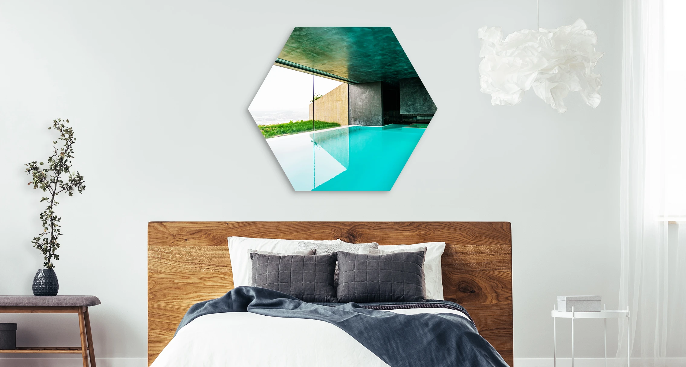 The overview of a pool with a view of the sea hangs in a hexagon format above a bed.