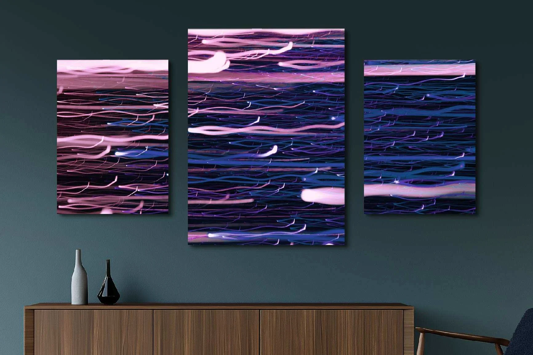 Trittico con linee astratte ondulate nei toni del rosa e del blu sopra una credenza con tre vasi davanti a una parete verde scuro.