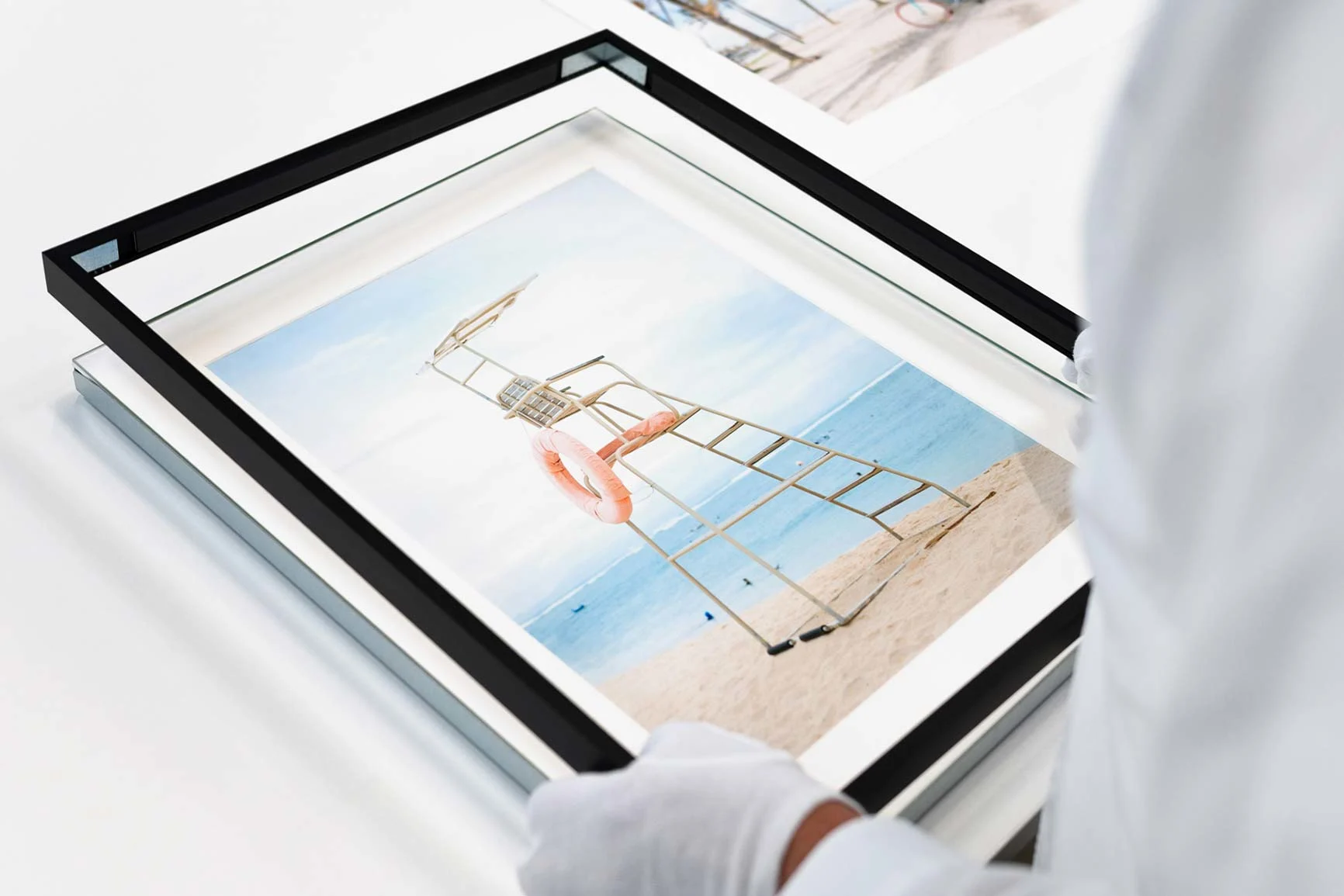 Cornice magnetica amovibile con una foto di una torre di salvataggio sulla spiaggia, incorniciata da una persona con guanti bianchi.