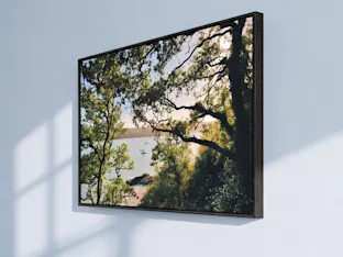Framed coastal landscape photo with trees and sailboats, hung above a walnut sideboard; close-up of dark wood frame detail shown.